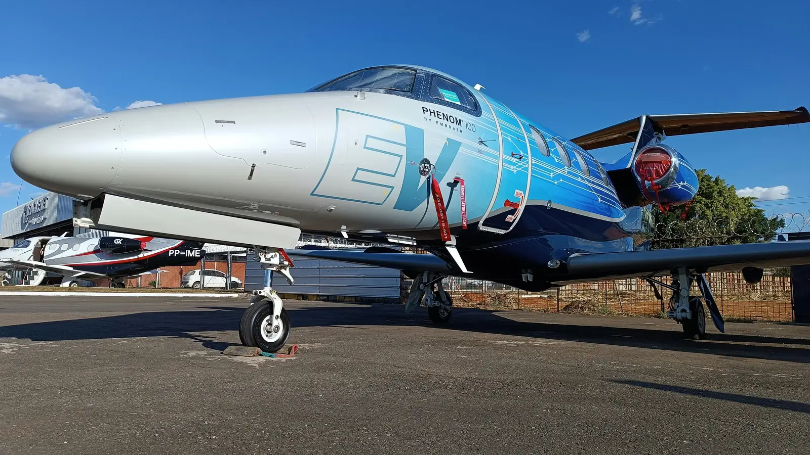 Embraer Phenom 100 light business jet parked on a sunny ramp with ground service equipment alongside
