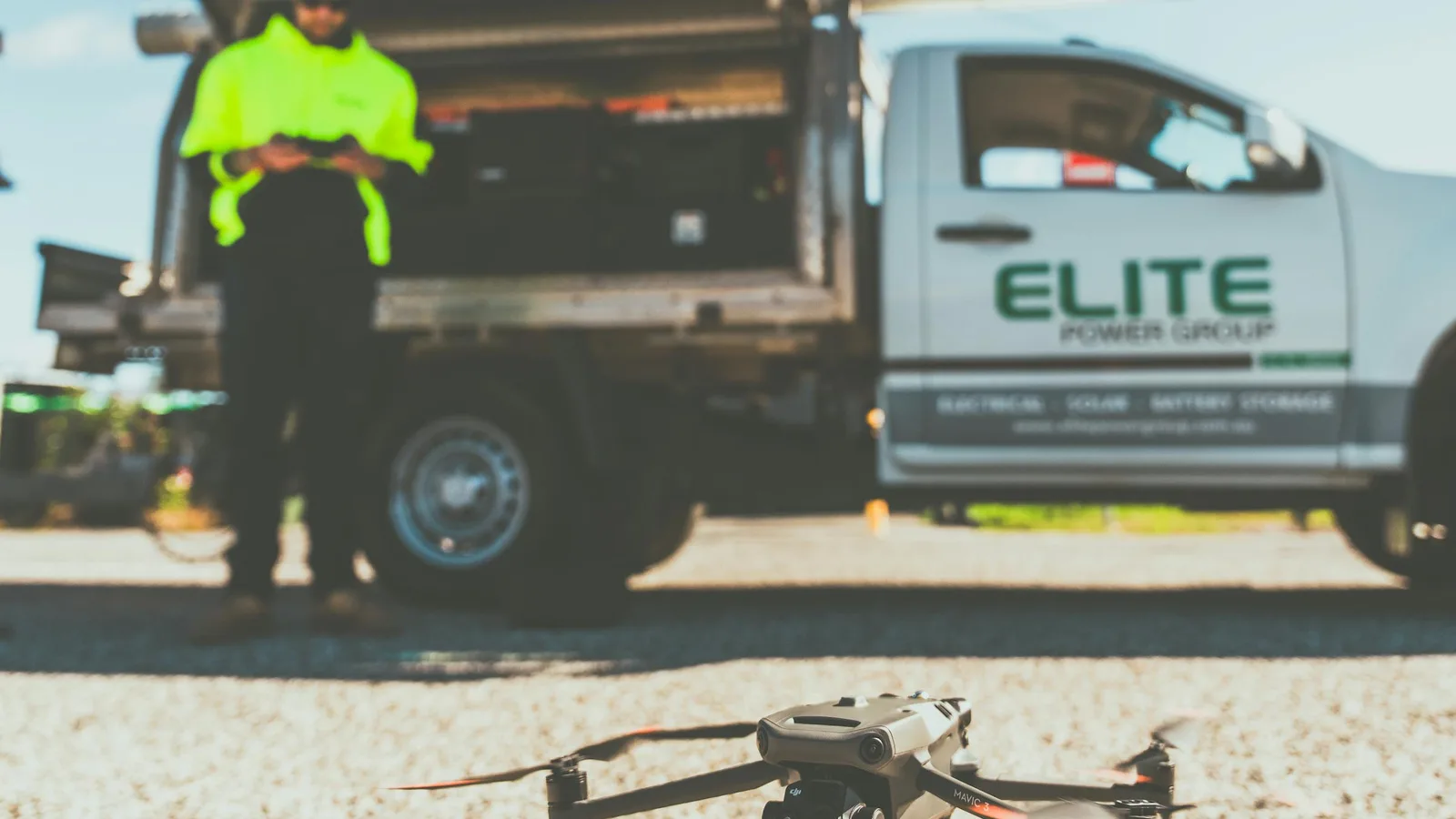 Hi-vis UAV operator launching a commercial drone beside a liveried utility truck on an industrial job site