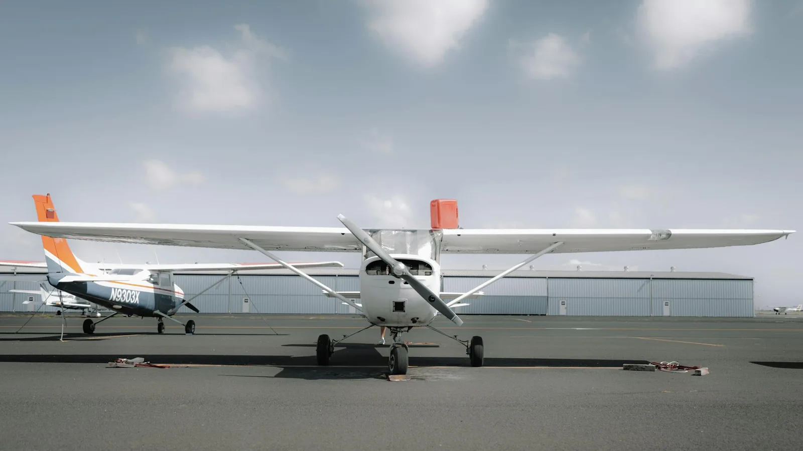 Single-engine high-wing piston trainer parked on the airfield ramp at a flight school