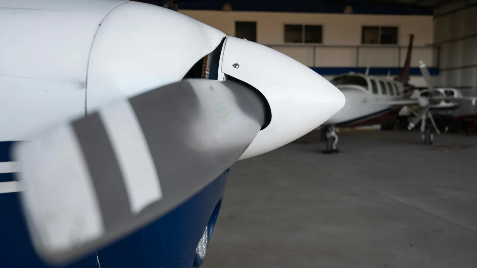 Business turboprop spinner and propeller blade in the foreground with cabin-class twins parked behind in a maintenance hangar