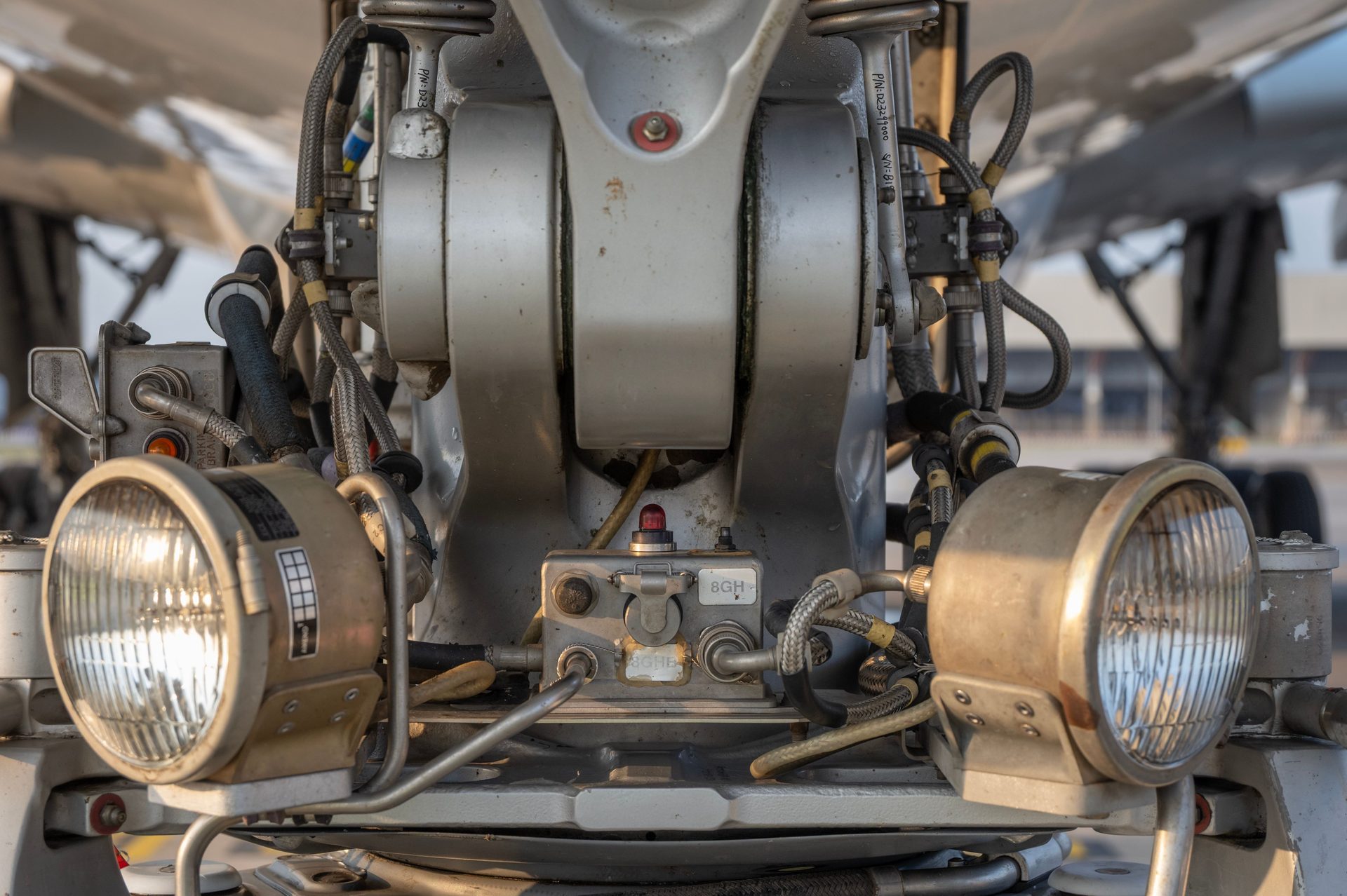 Aircraft nose landing gear strut with hydraulic lines and landing lights at golden hour